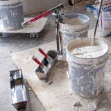 Level 5 joint knives in a mud pan, with a Level 5 mud pump and mud mixer in buckets of drywall compound on a jobsite floor
